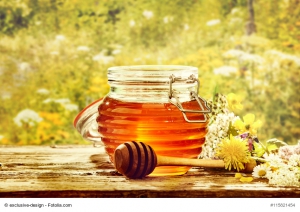 Bowl of honey with dipper in field of flowers